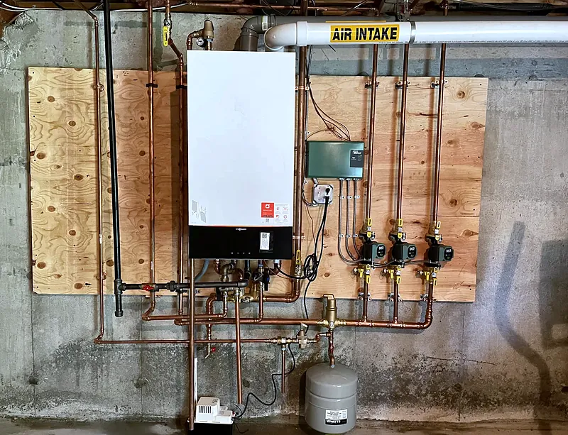 Viessmann wall-hung boiler on a plywood backboard with copper piping, three circulator pumps, and an expansion tank
