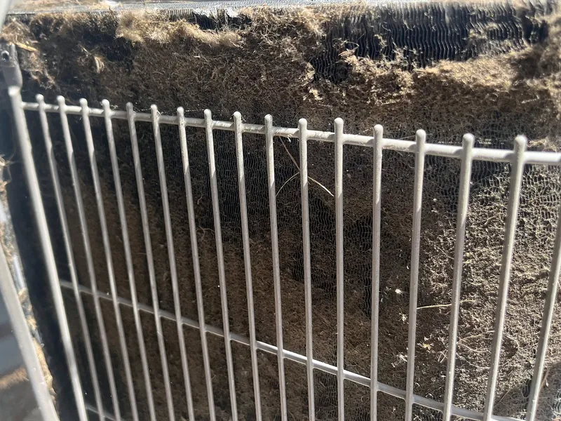 Debris packed into a condenser coil behind the wire guard