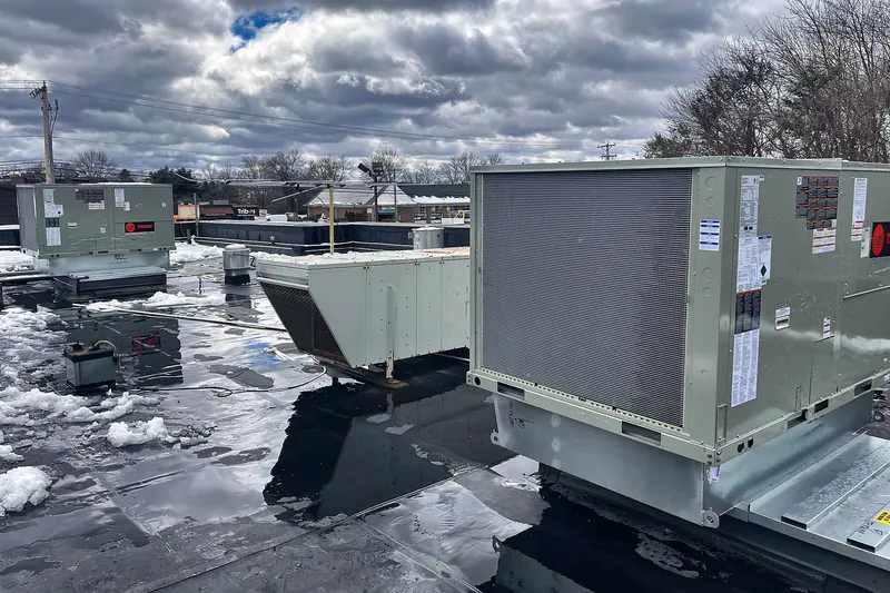 Two Trane packaged rooftop units on a flat commercial roof with melting snow