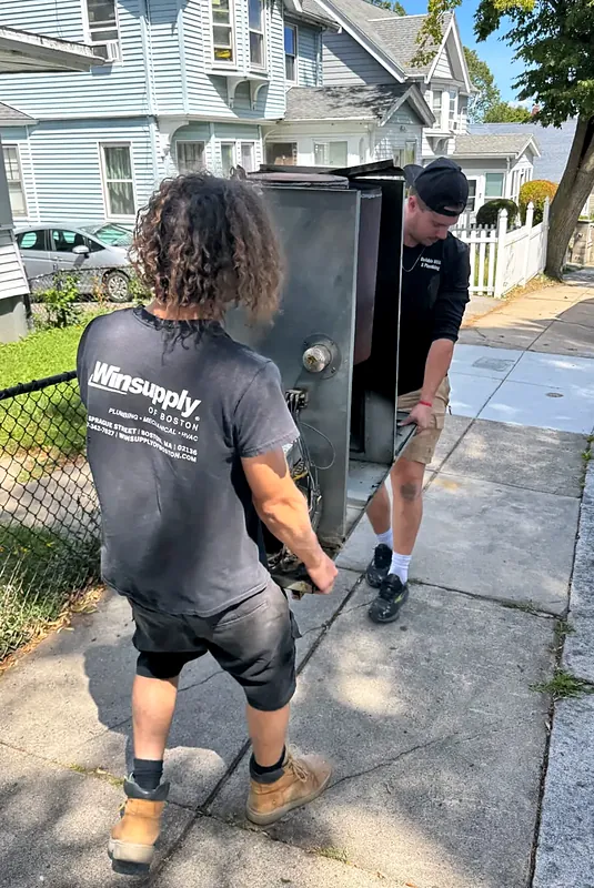 Two crew members carrying old equipment out of a house to the sidewalk