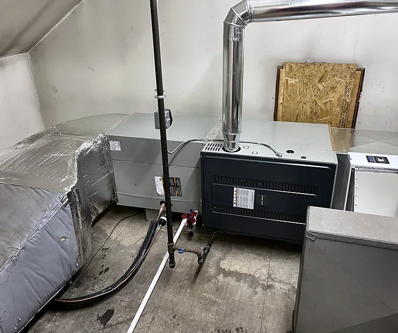 Gas furnace installed on its side with a stainless steel flue, connected to ductwork in a mechanical room