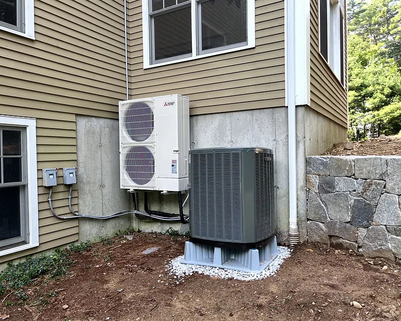 Mitsubishi Electric outdoor unit on a wall bracket beside a central air condenser on a stand