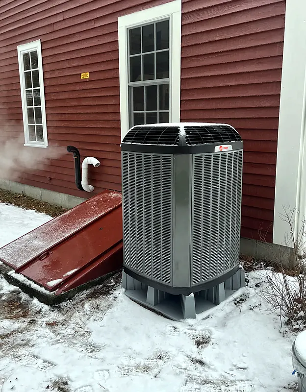 Outdoor unit beside a red house after a snowfall