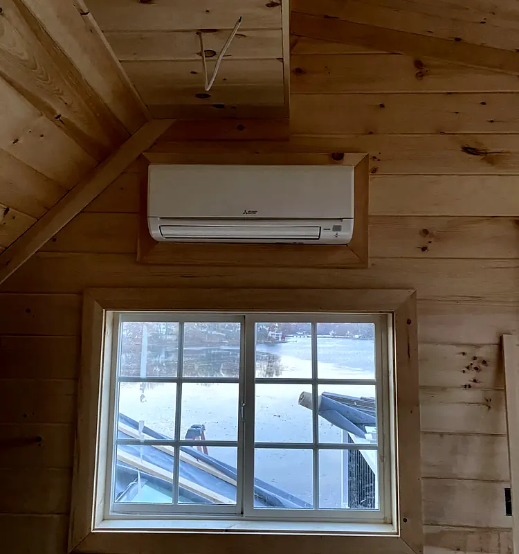 Mitsubishi Electric wall unit above a window in a pine-paneled room