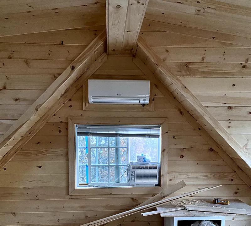 Mitsubishi Electric wall unit above a window in a pine-paneled room still under construction