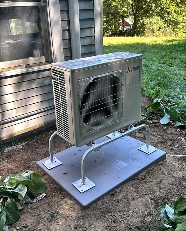 Mitsubishi Electric outdoor unit on a raised stand and pad beside a house