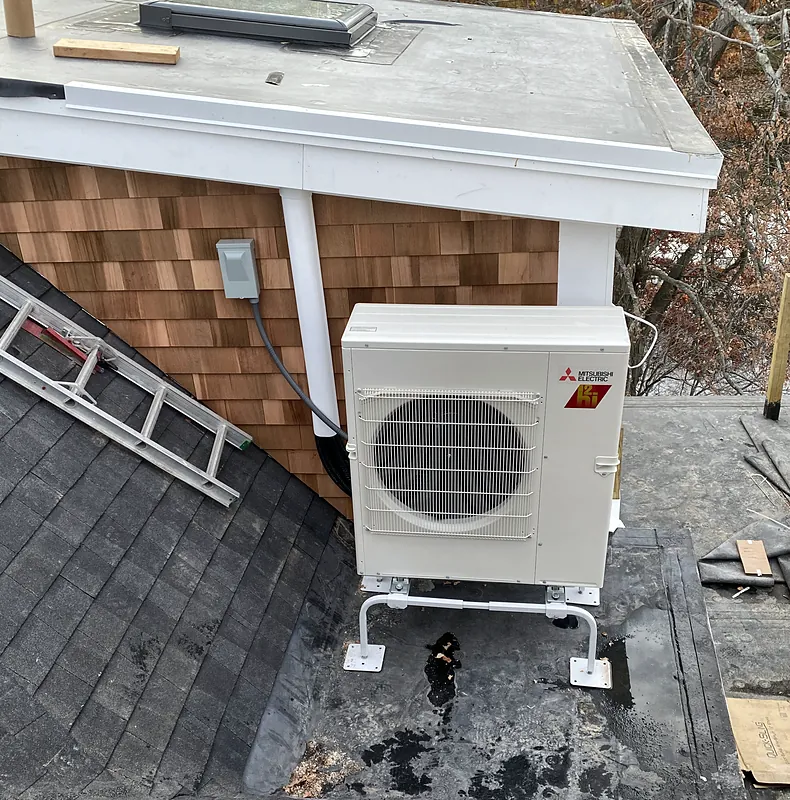 Mitsubishi Electric outdoor unit on a stand on a flat roof section beside a shingled roof