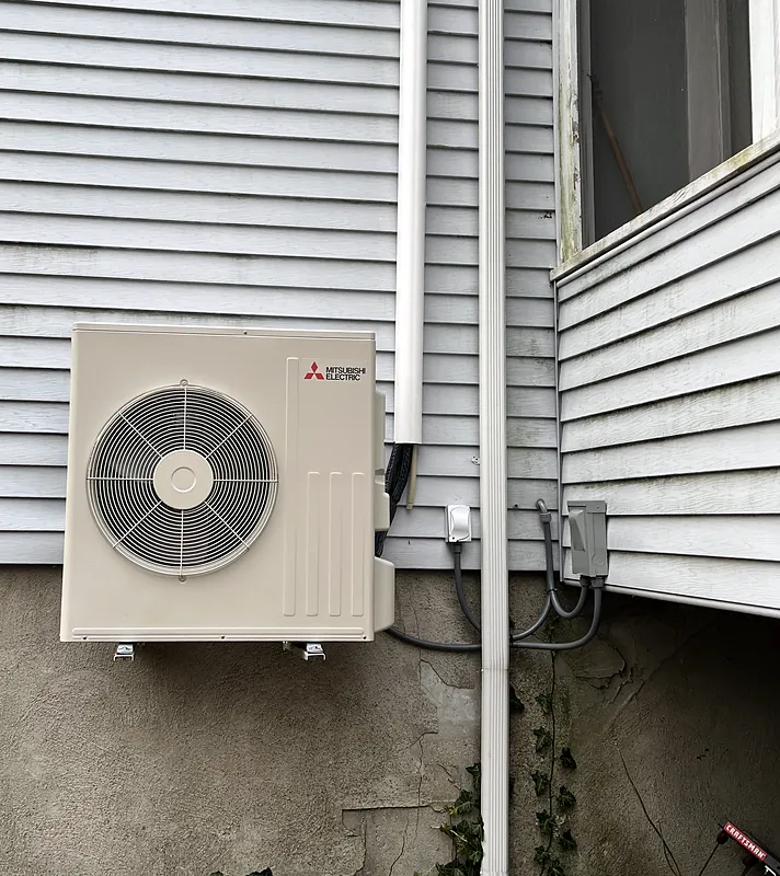 Mitsubishi Electric outdoor unit mounted on a wall bracket beside a house