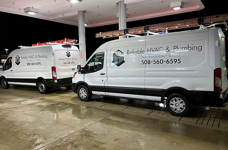 Two Reliable HVAC service vans with ladder racks, parked at night